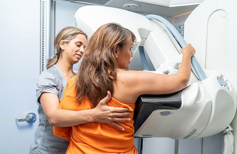 Woman is supported by technician to receive mammogram.