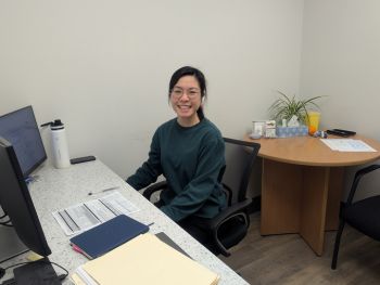 Woman with dark hair sits at a desk. 