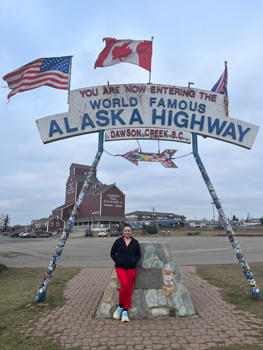 Woman standing underneath the Alaska Highway sign
