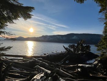 A sunset seen over mountains, ocean, and a pile of driftwood