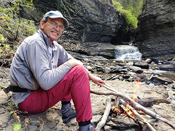 Man sits by stream with small waterfall in background