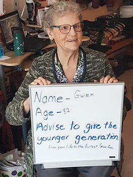 An older woman holds a white board sign offering advice for youth