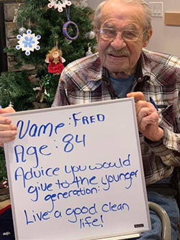 An older man holds a white board sign with advice for youth