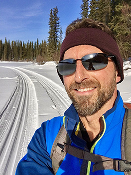 Man in sunglasses and toque stands with winter background