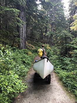 Man with backpack pulls canoe along dirt pathway