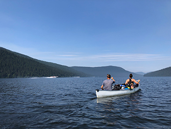 Two people paddle a canoe in a lake with airplanes in background