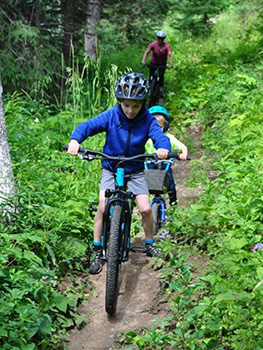 family rides bikes on a trail through the forest