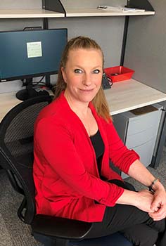 a woman with blonde hair in a pony tail wearing bright red blazer sits at a desk