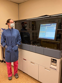 Woman stands next to large lab equipment 