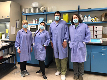 Four lab workers pose in lab with their protective garments on