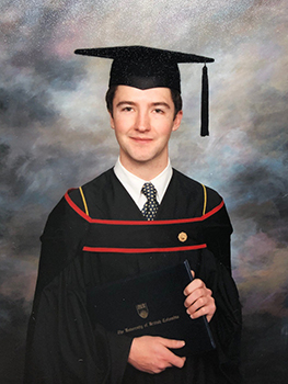 Young man in graduation cap and gown poses with diploma