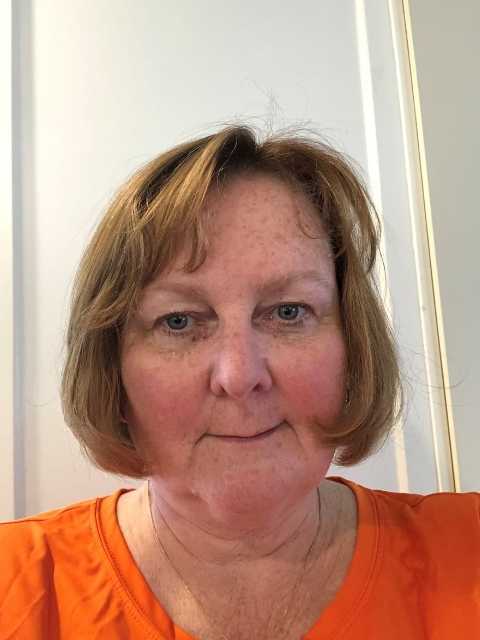 selfie of a woman with blonde hair wearing an orange shirt 