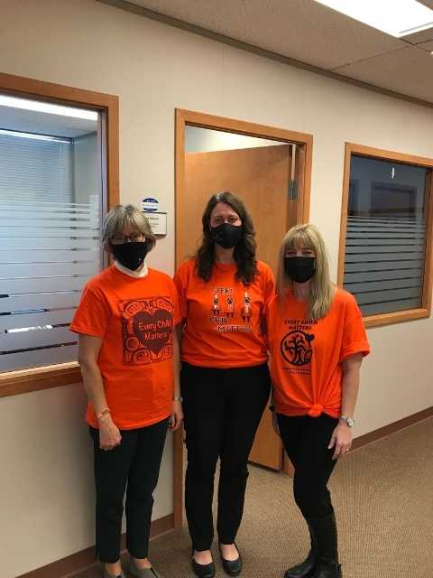 three women standing in a row wearing orange shirt day shirts