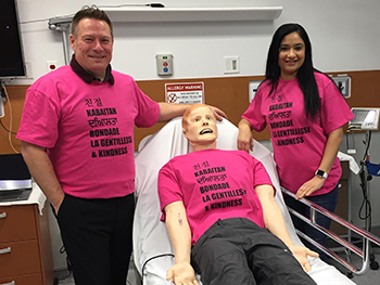 Two people stand on either side of a hospital bed wearing pink shirts. 