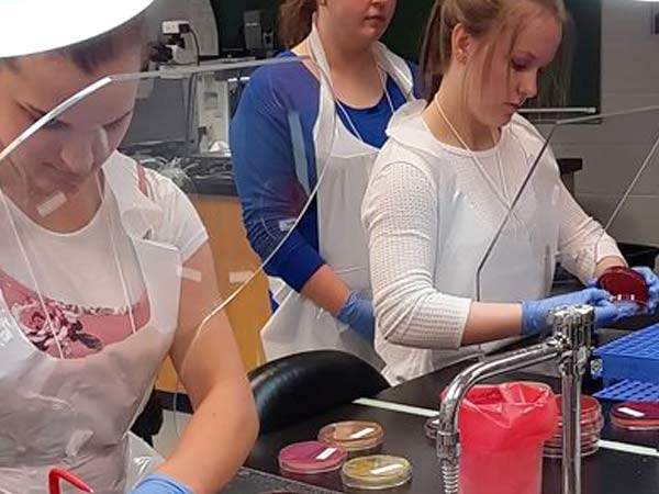 Two high-school students try hospital lab work under the supervision of a professional.