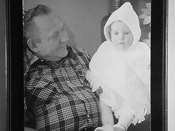 Black and white photo of older man holding a baby in a knitted outfit