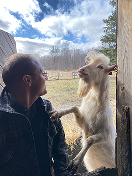 Man sits near barn window with goat