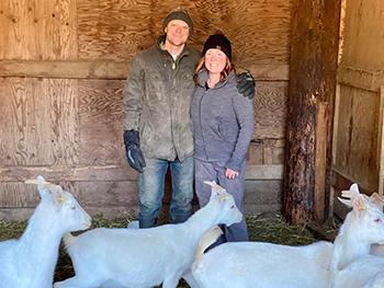 Couple stand in barn with white goats