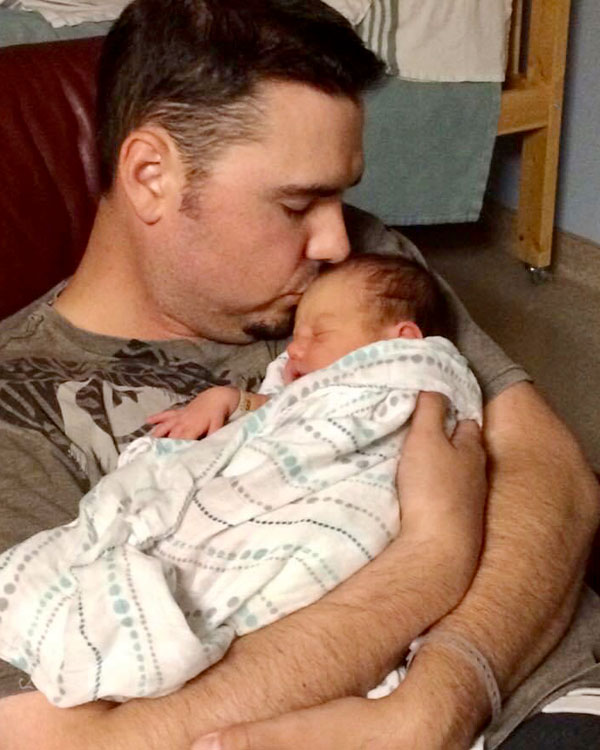 A man cuddles his newborn, kissing it on the head.