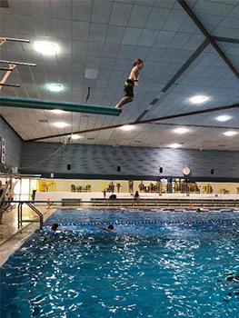Child jumping off diving board at community indoor pool.