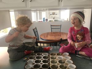 Two children sitting on the counter with muffin tins. 