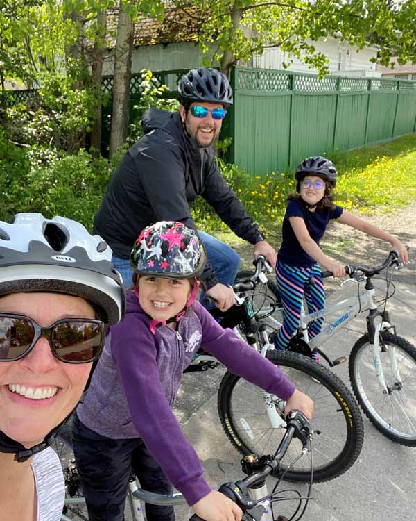 A mother, father, and two daughters sit on their bikes, smiling.  