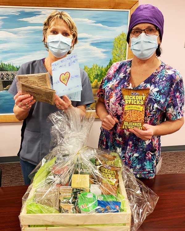 Two nurses wearing masks hold up a gift basket.