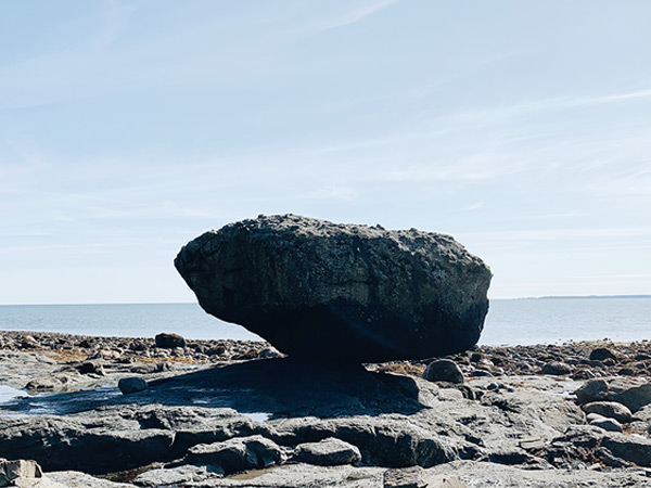 A large rock balances on a beach.