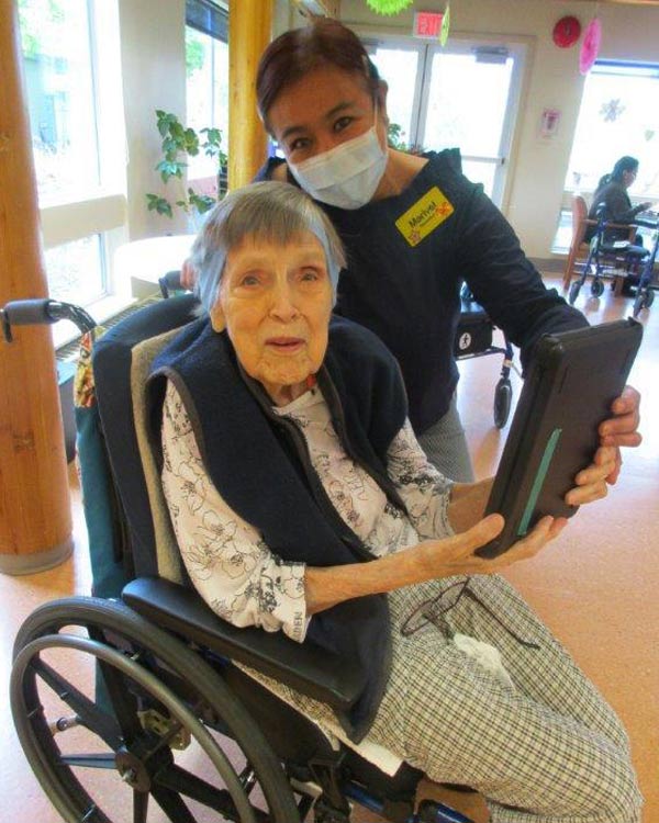 An elderly woman in a wheelchair and a female health care worker operate an iPad. 