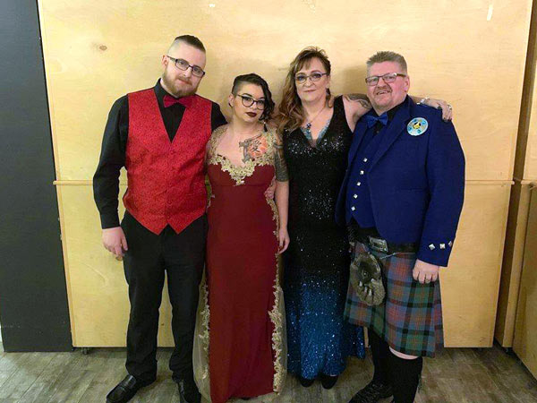 Man dressed in a Scottish kilt standing with his wife and two children.