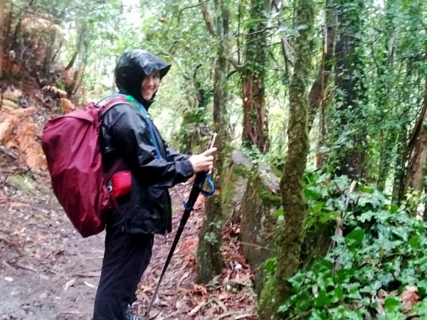 A woman in rain gear hikes in wet weather and smiles into the camera. 