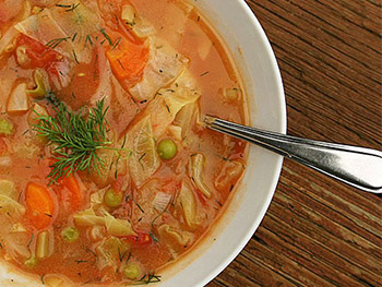 Soup with carrots, dill, cabbage, peas in a white bowl.