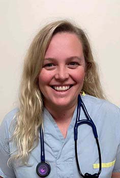 a young blond woman wearing light blue scrubs with a stethoscope around her neck smiles into the camera