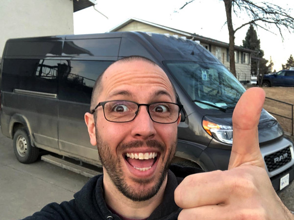 A man with glasses, a shaved head, and a beard smiles and gives a "thumbs up" to the camera.