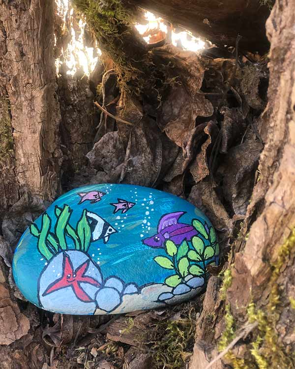 A rock has an underwater ocean scene painted on it with seaweed, fish, and a star fish. 