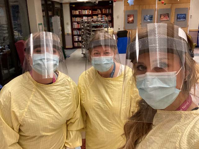three health care workers pose for a selfie in full PPE