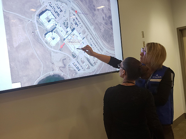 Two women look at a Google Earth view of a building on a projection screen.