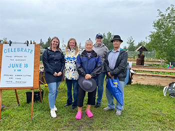 A group of people stand next to a sign that notes a garden opening