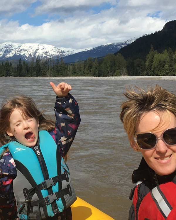 Gillian and her four-year-old daughter, wearing life jackets, in a boat on the Skeena River. The river, forest, and mountains are behind them.