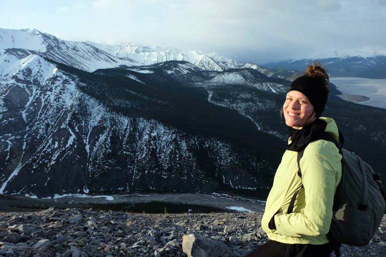 Woman standing at a viewpoint with snow capped mountains in the distant and a valley below.