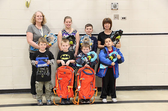 Students and 2 teachers standing with backpacks and snowshoes.