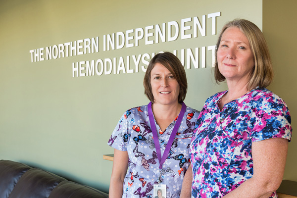 Two women wearing brightly colourled top standing against a wall.