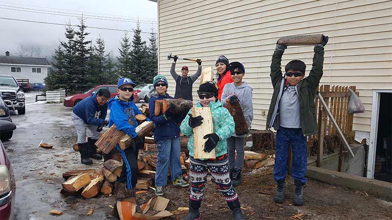 Kids helping elders cutting wood beside a house during winter.