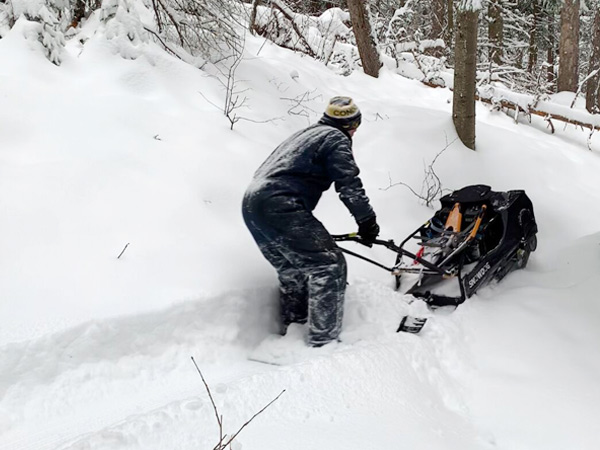 A person cuts a trail out of the snow using a trail making machine.