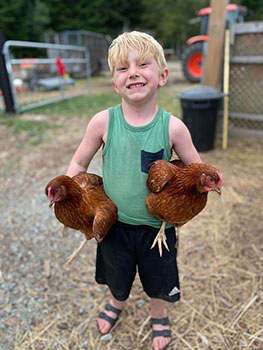 Small child carries two chickens under his arms