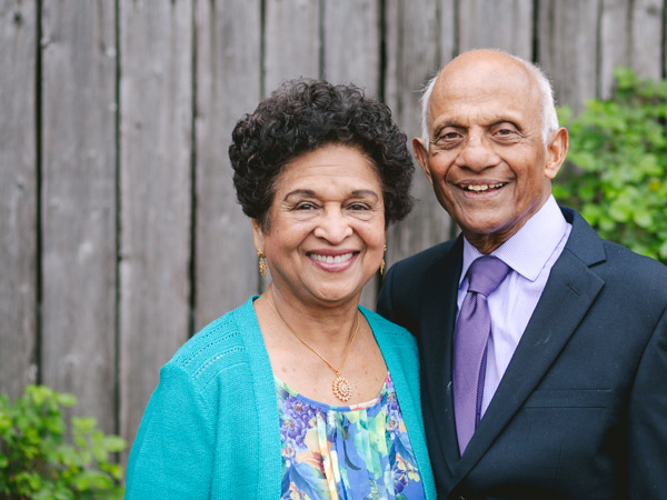 An senior man and woman stands in front of a fence smiling.