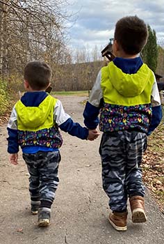 two young boys wearing matching yellow and blue coats hold hands