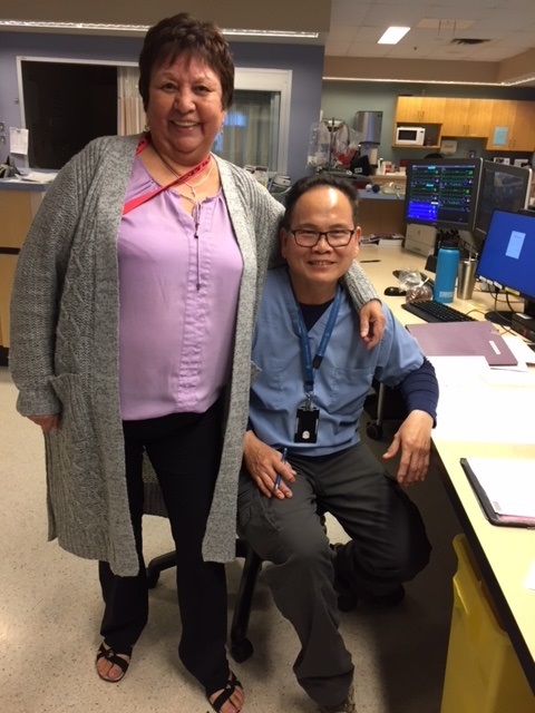 A male sitting and female health professional standing and smiling while facing the camera