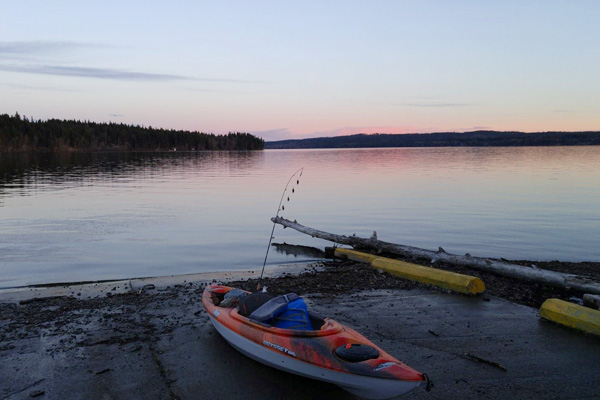 A kayak with a fishing rod on the beach at West Lake at sunset.