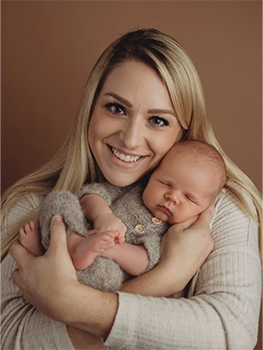 young blonde woman smiling into camera holding small baby